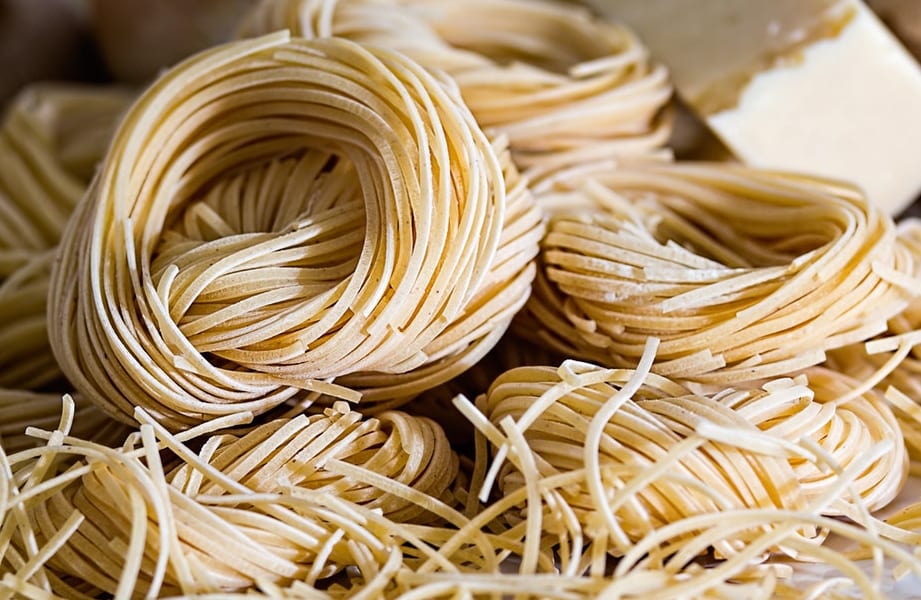 dried capellini pasta bundles with a block of parmesan and shallots