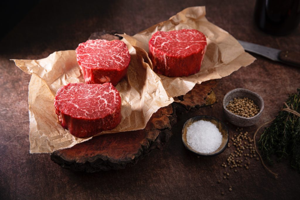 Three filet mignon steaks on butchers paper on a wooden cutting board with finger bowls of salt and pepper beside them; relating to the perfect classic date night dinner.