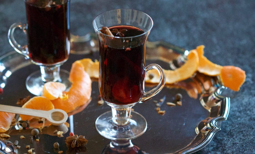 closeup of two glass cups with handles holding mulled wine, on a silver planned with orange rinds and raw spices; highlighting Heavens Gate Winery Holiday Wine Pairing