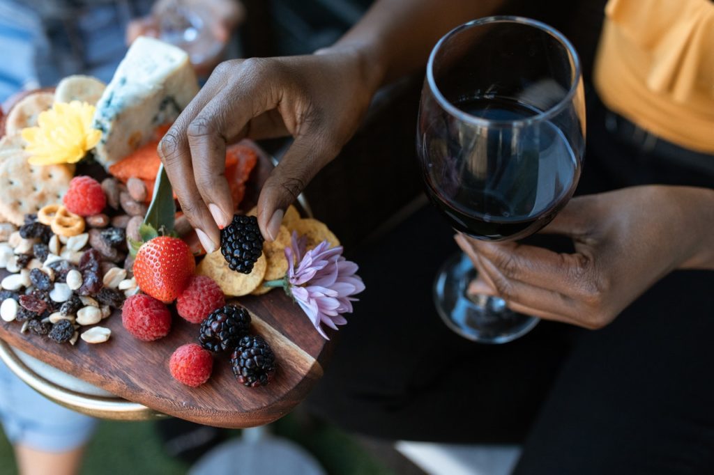 closeup of a woman holding a wine glass and a blackberry from a charcuterie board, highlighting a guide to okanagan food and wine pairing